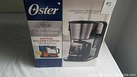 Front view of the Oster 12 cup programmable coffee maker in original packaging showing branding and product image.