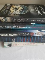 Stack of five fictional paperback books showing titles and authors on the spines.