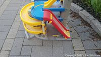 Plastic multi-level toy garage with yellow curved ramp and red straight slide with some dirt visible on ramps.