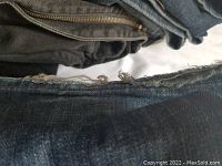 Close-up image showing dark denim jeans with frayed hems and worn fabric, indicating use.