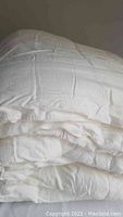 Photo of folded white comforter showing texture, quilted design, and staining.