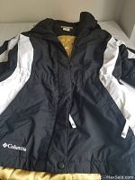 Full view of the black and white Columbia women's jacket laid flat, showing front zipper, sleeves, and collar with yellow lining visible inside.