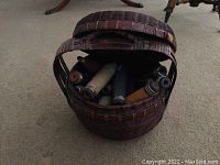 Round wooden basket with handle and removable lid visible on carpet with some wooden spools inside.