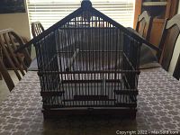 Full front view of antique bird cage in wooden and metal construction, placed on dining table.