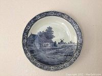 Blue and white ceramic plate featuring cottage and windmills scene with detailed border pattern.