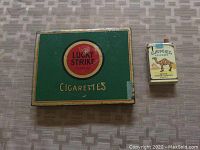 Top view of green metal Lucky Strike cigarette box and Camel cigarette lighter showing front designs.