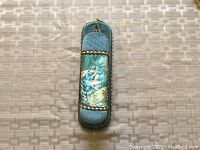 Front view of hanging brush showing blue textured handle with decorative painted scene of a couple and metal bead embellishments