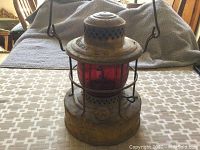 Full view of antique kerosene lamp showing red glass globe, metal handle and rust on metal body.