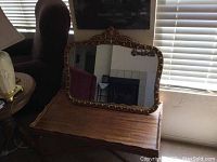 Front image showing the vintage rectangular mirror with a decorative gold-tone frame featuring raised golden rose accents, placed on a wooden surface.