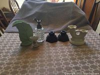 Full view of 4 candle holders, perfume bottle, and flower vase on a table covered with a patterned cloth