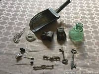 Overall photo showing all items including metal scoop, keys, clips, pins, brooch, and glass ink bottle spread out on a patterned surface.