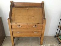 Closed old wooden desk showing drop-front panel, two small drawers above a larger drawer, and four legs.