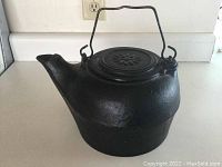 Photo of an old black metal water kettle with a wire handle and a star design on the lid.