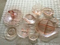 Overview photo showing all eight pink glass dishes laid out on a patterned tablecloth, displaying various shapes and sizes of vintage glassware.