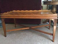 Front view of the wooden coffee table showing scalloped edge tabletop and crossed stretcher legs.