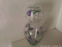 Clear glass vase featuring purple painted flowers on body and rim.