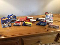 Wide view of all toy trucks and packaged Hot Wheels cars on wooden surface.