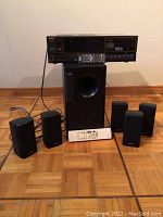 Full lot with Sony A/V control center atop Bose subwoofer, five Bose satellite speakers arranged around, and two remote controls placed in front.