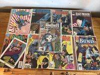 Photo of the full set of 9 Batman and one Punisher comic books laid out on table, showing front covers with varying Batman artwork and visible wear.