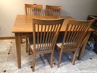 Rectangular light wood dining table with four matching chairs in kitchen setting.