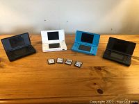 Four Nintendo DS consoles in various colors with four Nintendo DS game cartridges in front