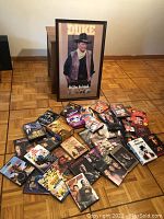 Photo showing collection of DVD movies spread on floor in front of a framed western-themed Duke poster.
