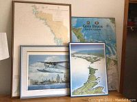 Four framed art pieces including maps and a seaplane print arranged leaning against a wall.