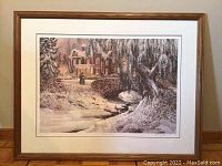 Framed art print in wooden frame with visible scratches, depicting a winter house scene with bridge and creek.