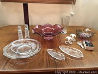 Full view of all glassware and crystal items on wooden table showing purple ruffled-edge bowl, clear plates, candle holders, and decorative mushroom pieces.