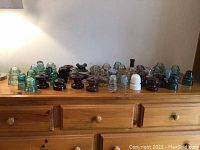 Group of about 40 vintage insulators in various colors and shapes arranged on wooden dresser.