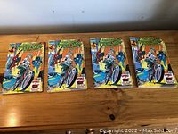 Four copies of The Amazing Spider-Man comic displayed on a wooden surface showing front covers.