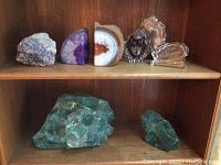 Top shelf showing purple amethyst geode slice, brown and white banded agate slice, and three clear crystal paperweights with animal and text designs.