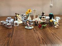 Full view of lot on wooden table showing cups, figurines, vases, and other decorative items.