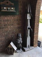 Wide angle showing three outdoor decor items together against brick wall: bear statue, vintage water pump, and insect house.