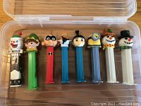 Top view of 8 character PEZ dispensers lined up inside a clear plastic box.