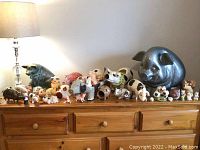 Wide photo showing a dresser top filled with various pig figurines and sculptures of different sizes and materials, highlighting the variety in the collection.