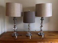 Front view of all three lamps showing chrome and crystal bases with fabric shades in beige and gray.