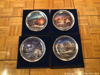 Four Terry Redlin collector plates displayed in original blue velvet-lined boxes on wood floor, showing artwork with winter and rural scenes.