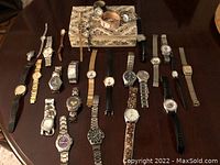 Full lot showing 19 assorted wristwatches of various styles, bands, and dial designs, arranged on wood surface and raised covered platform.