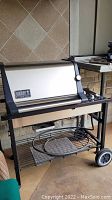 Full view of Weber Genesis Gold BBQ grill showing stainless steel lid, side shelves, and lower racks with grill grate and warming rack.