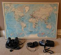 Photo showing the entire lot with the framed Political World map and three pairs of binoculars placed in front of it. The map is large with a wooden frame; binoculars include Bushnell Off Trail 10x30, Sharper Image compact 8x21, and Kenko 8x-20x50.