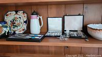 All items displayed on shelf showing decorative plate, vase, stein, serving utensils, sterling spoons, glass pumpkin and bowl