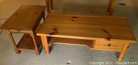 Photo showing both pine tables on carpet. Coffee table is rectangular with drawer and lower shelf; end table square with drawer and lower shelf.
