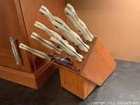 Wooden Cutco branded knife block on countertop showing white-handled knives