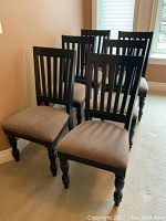 Six black wooden dining chairs arranged on carpet near windows showing vertical slat backs and beige cushioned seats