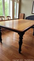 Full side angled view of the wood dining table showing rounded edges and wood grain top surface with black turned legs.