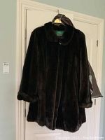 Full view of mid length dark brown fur coat hanging on a door.