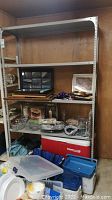 Full view of assembled gray metal shelving unit with four metal shelves containing various items (not included in lot). Located in basement.