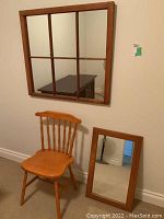 Large wood frame window pane mirror mounted on wall above wooden chair and smaller rectangular mirror leaning on wall.