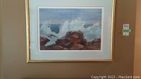 Full view of framed painting showing lake waves splashing on rocks with white spray and soft sky.